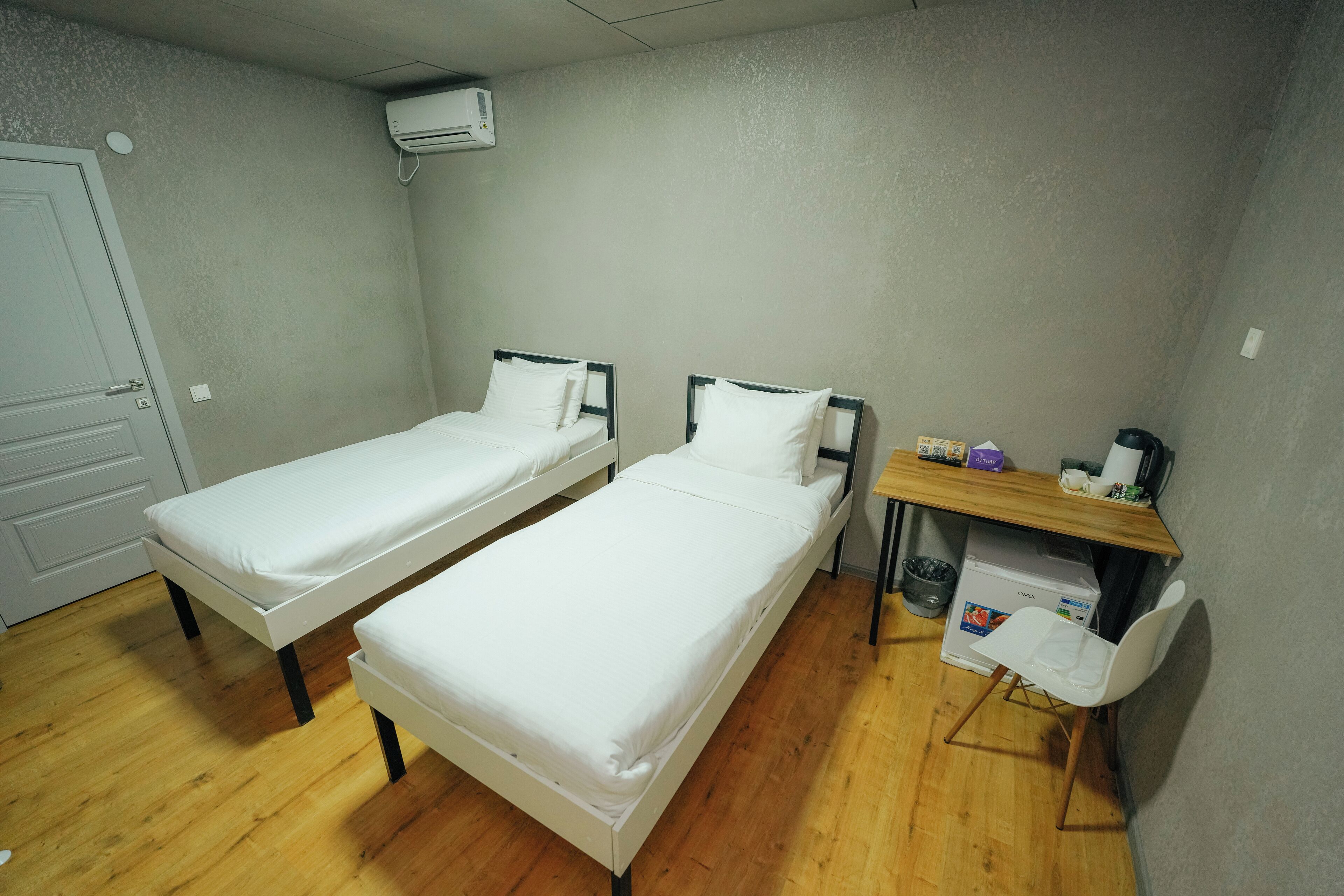 Een kamer met twee éénpersoonsbedden, een houten vloer, een tafeltje met een stoel en een airconditioner aan de muur.