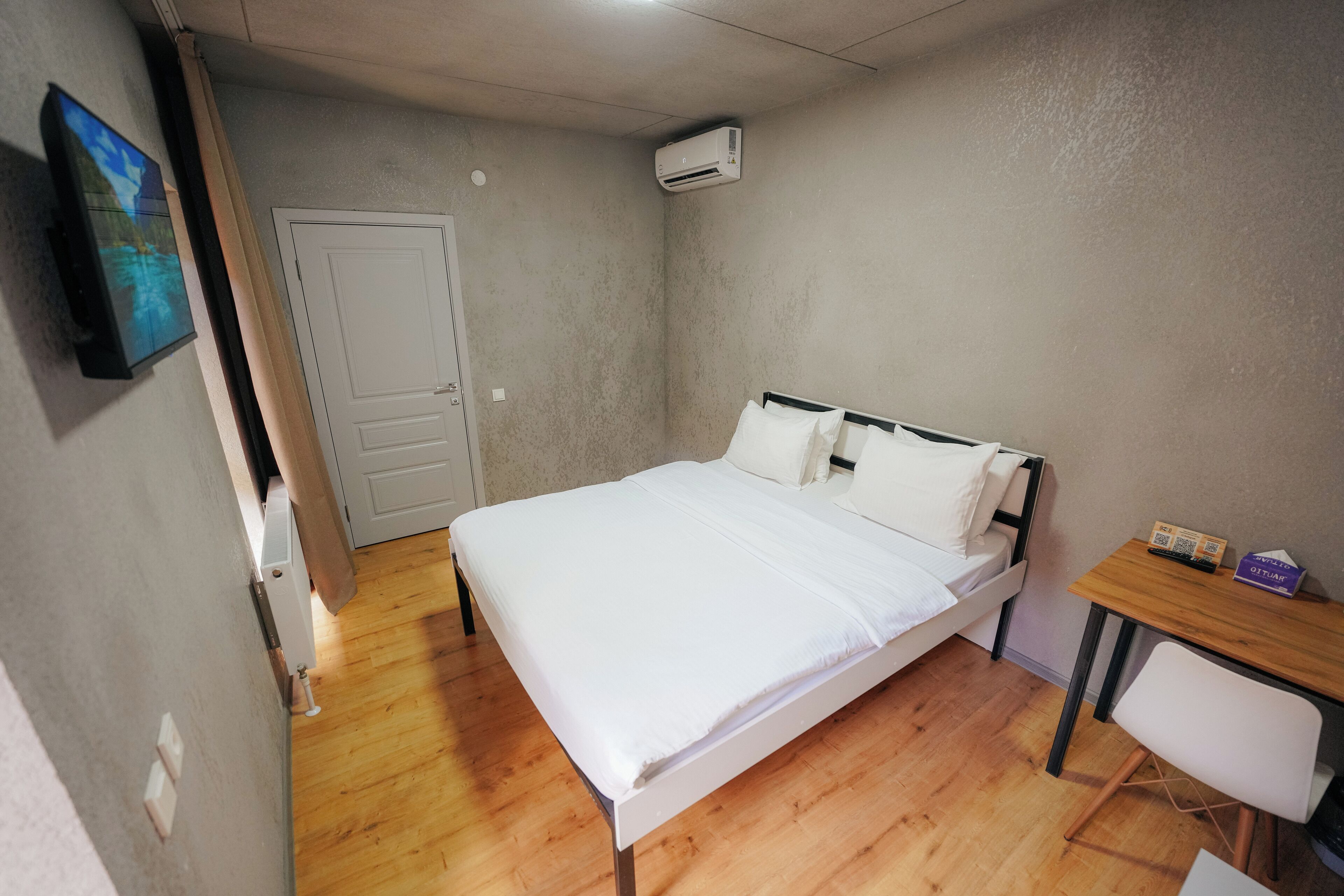 A bedroom with a bed, a desk, and an air conditioning unit.