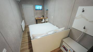 A hotel room with a bed, a desk, a chair, a TV, and a wardrobe.
