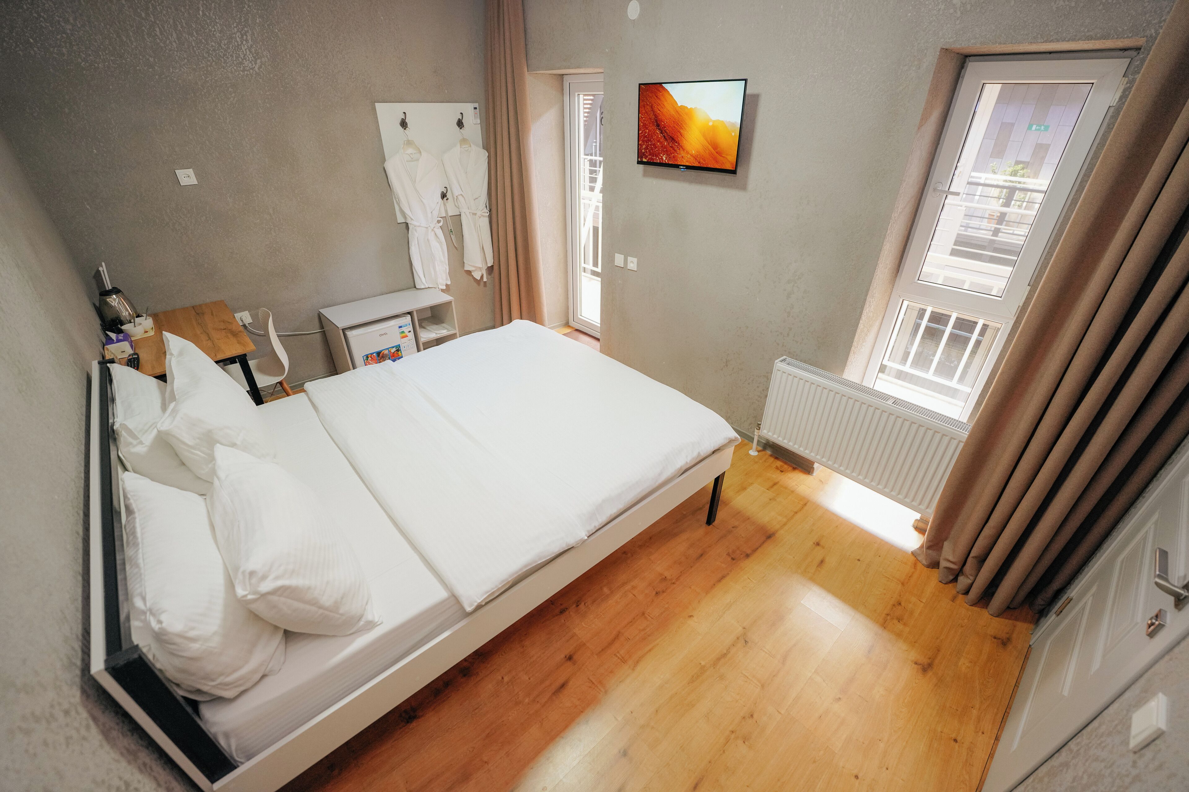 Un dormitorio con cama, escritorio, radiador y televisor en la pared.