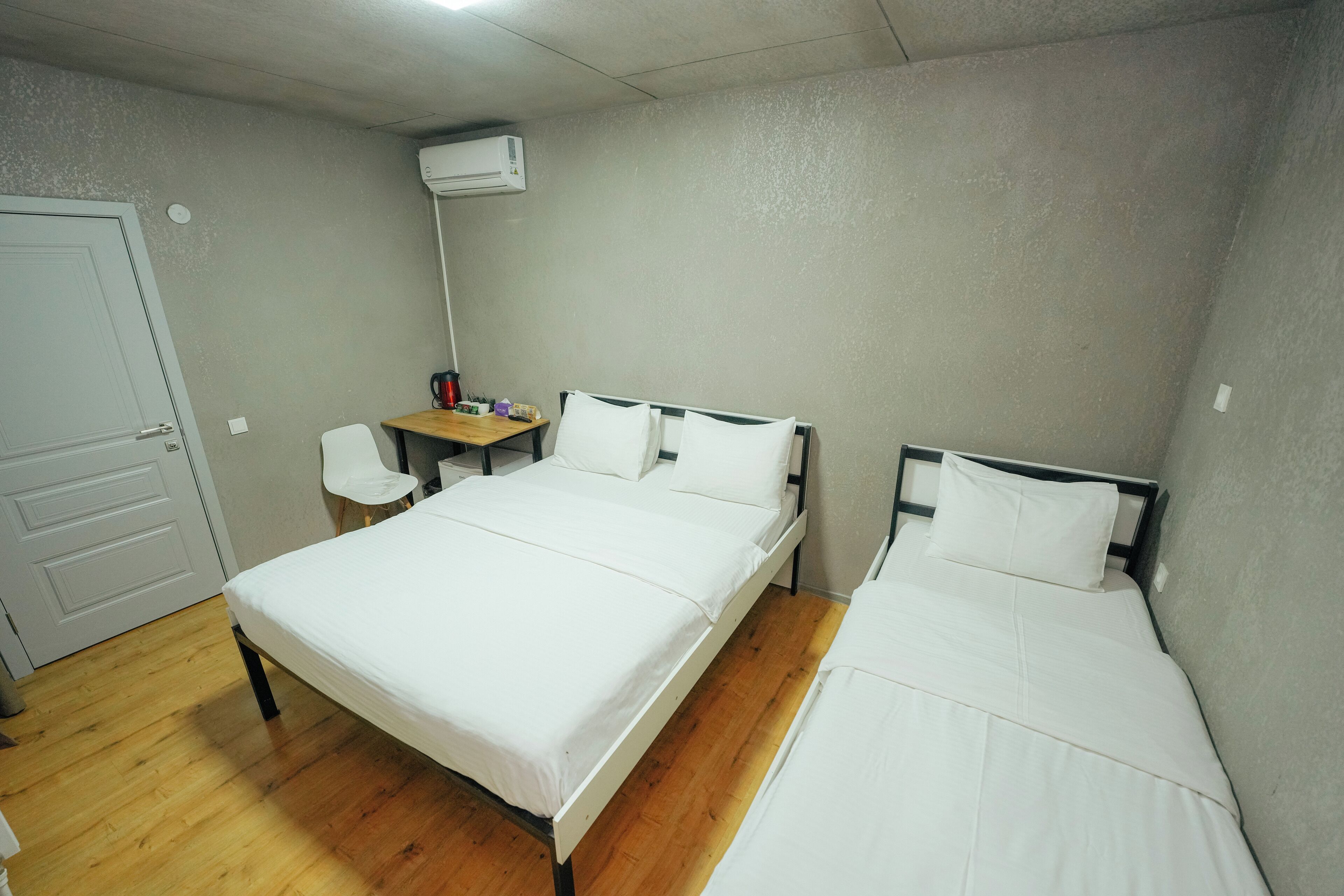 A room with two beds, a desk, a chair, and an air conditioning unit.