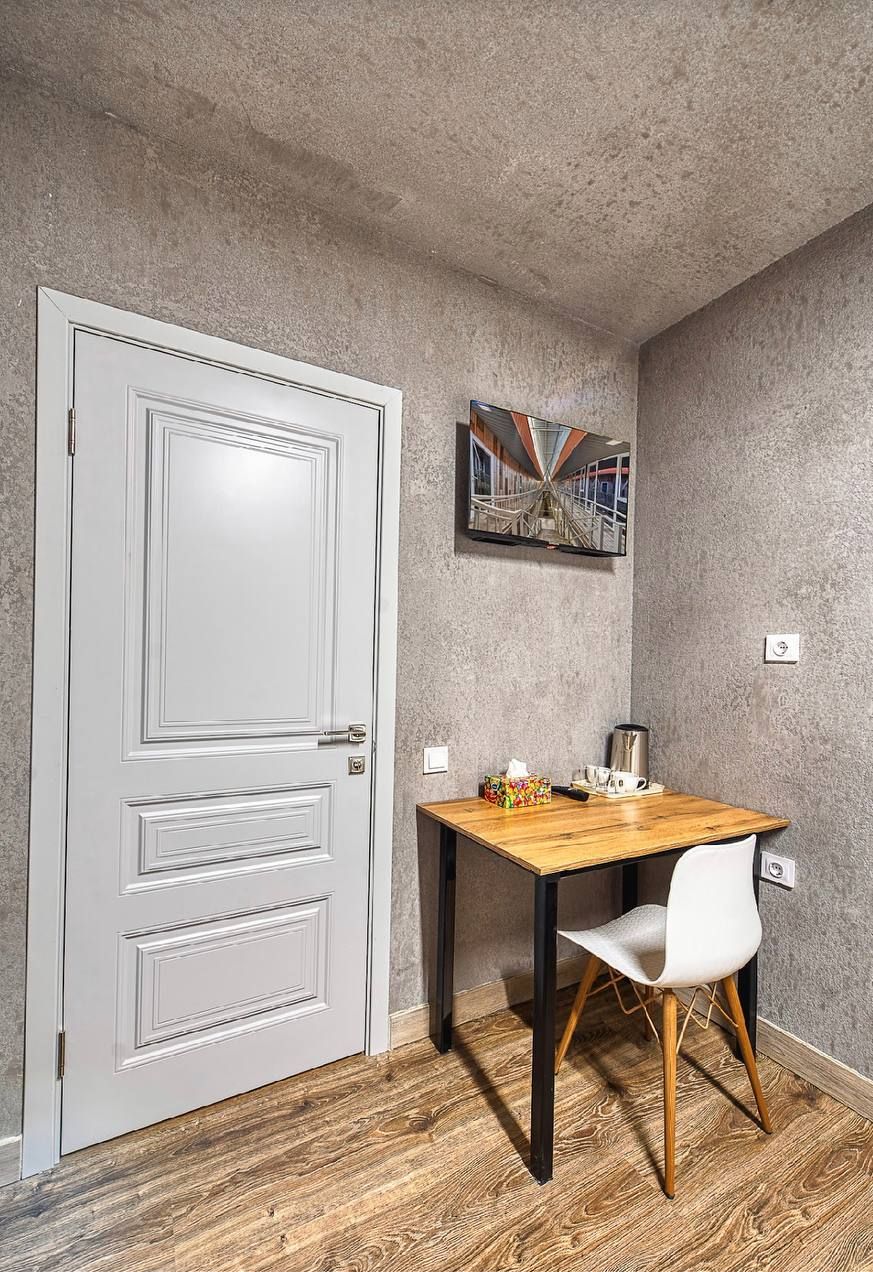 Una habitación con una puerta blanca, una mesa de madera con una silla blanca, un cuadro en la pared y una pared gris con textura.