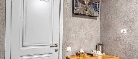 Una habitación con una puerta blanca, una mesa de madera con una silla blanca, un cuadro en la pared y una pared gris con textura.
