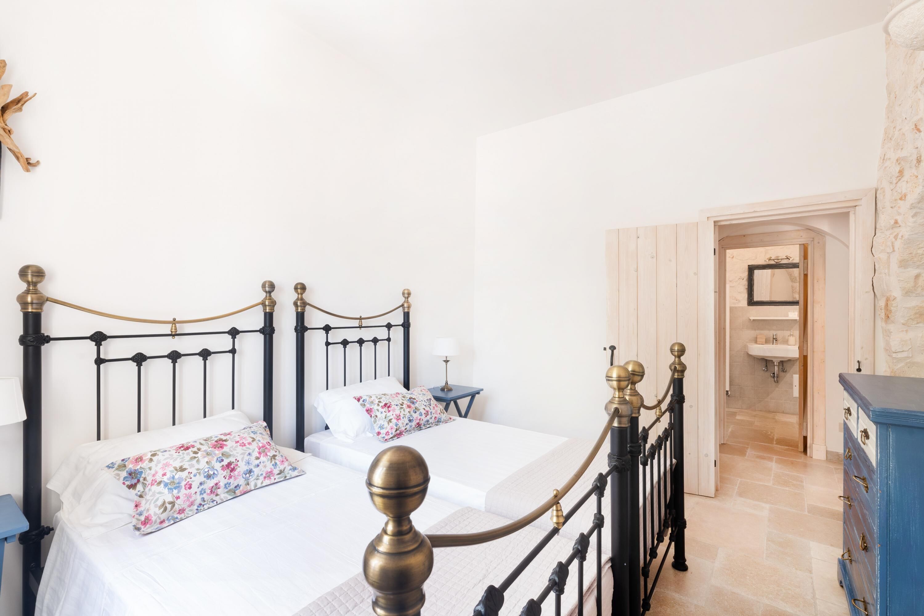 A bedroom with two beds, a nightstand, a dresser, and a bathroom visible through an open door.