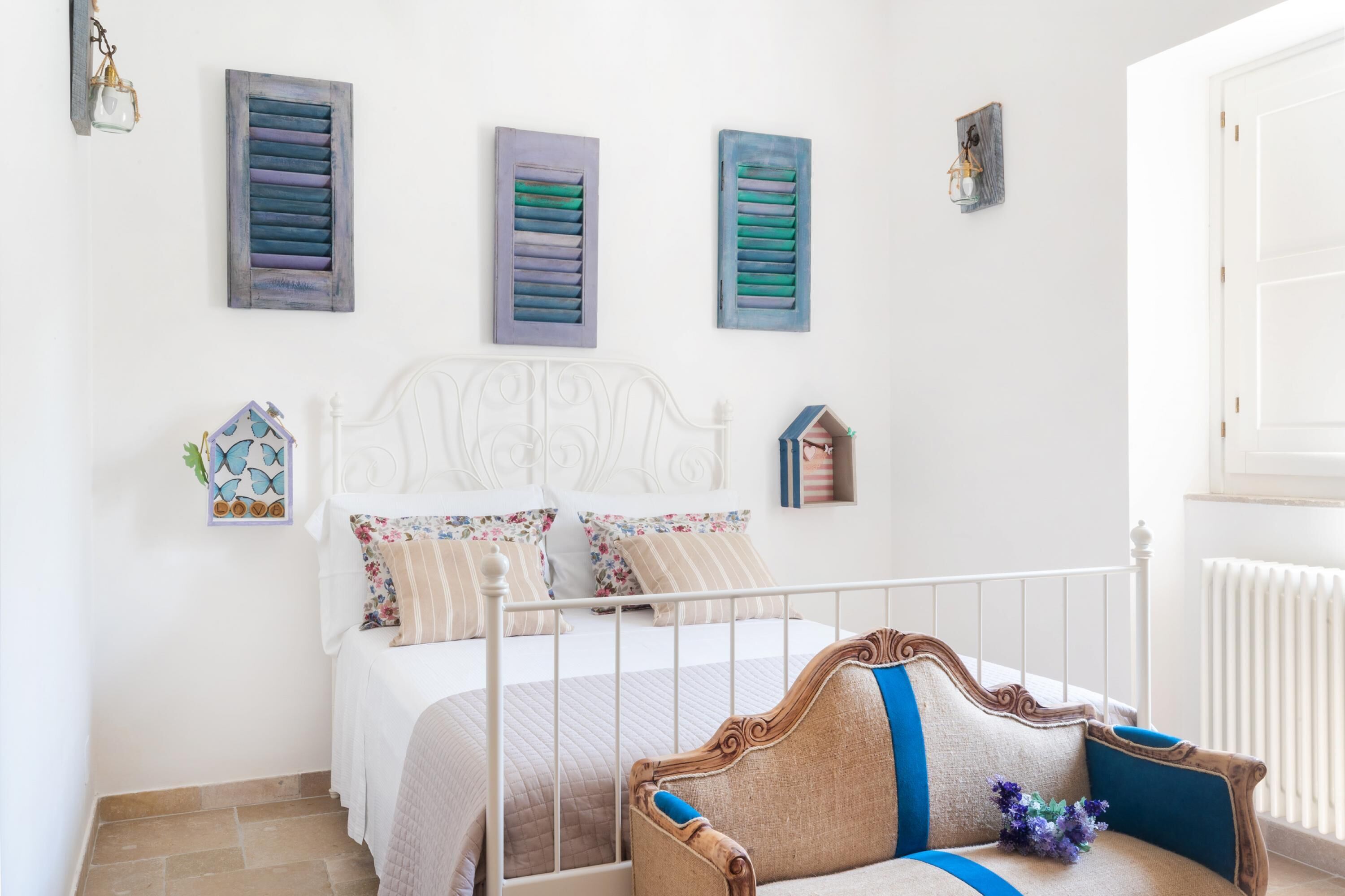 A bedroom with a white metal bed frame, floral-patterned bedding, and decorative wall art.