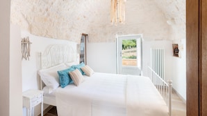 A bedroom with a white bed, a wooden headboard, and a view of the outdoors through a door. - Donna Vincenza in Selva di Fasano (Monopoli)