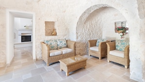 A cozy lounge area with wicker furniture, a stone wall, and a fireplace. - Donna Vincenza in Selva di Fasano (Monopoli)