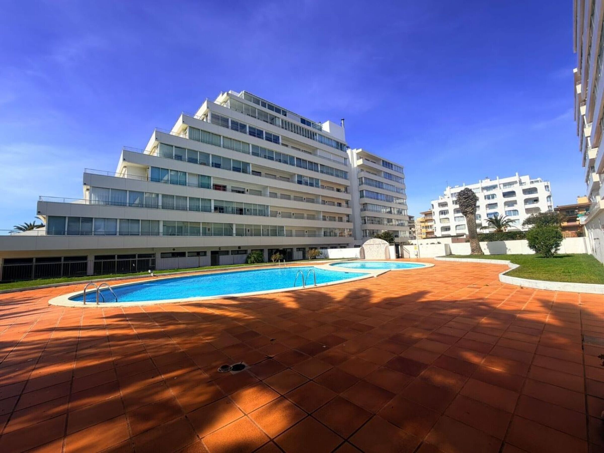 A modern hotel with a swimming pool, multiple floors, and a clear blue sky.