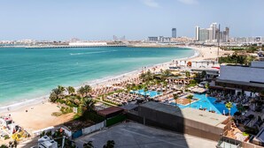 A coastal hotel with a beach view, a swimming pool, and a city skyline in the background. - Elite 2BR at La Vie with sea view (Dubai)
