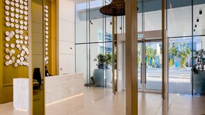 A modern lobby with a reception desk, glass doors leading outside, and a large potted plant. - Elite 2BR at La Vie with sea view (Dubai)