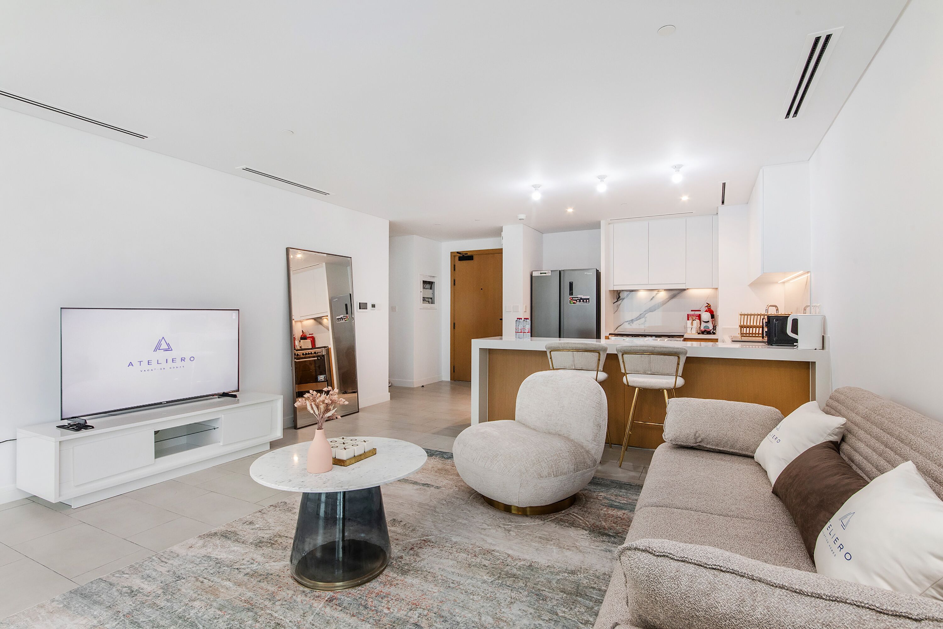 A modern living room with a flat-screen TV, a sofa, a coffee table, and a kitchen area in the background.