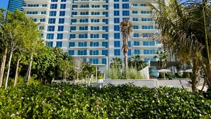 A tall, modern hotel with a white facade and blue windows, surrounded by greenery and palm trees. - Elite 2BR at La Vie with sea view (Dubai)