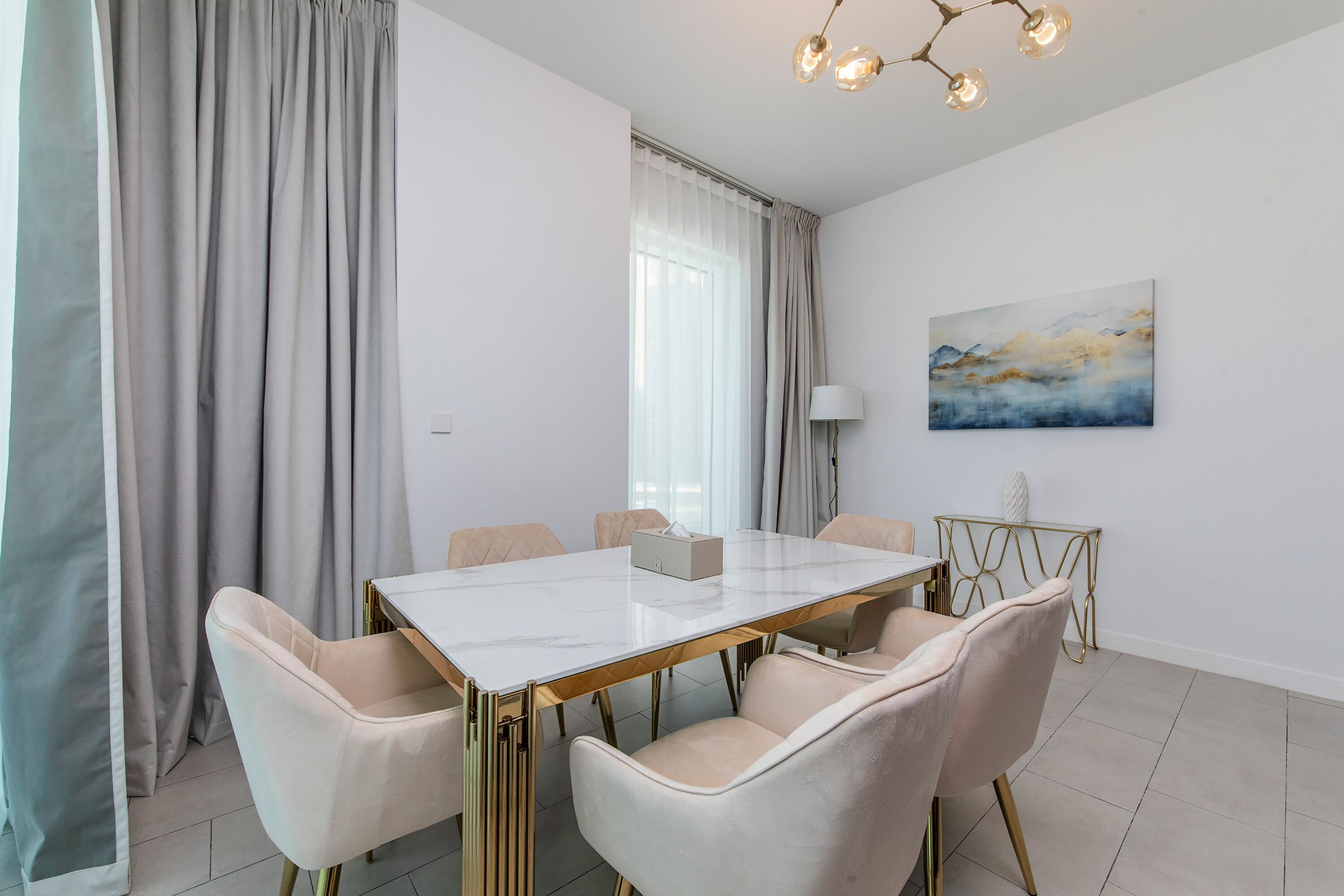 A modern dining room with a marble table, six chairs, a chandelier, and a painting on the wall.