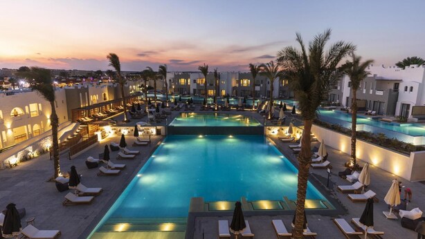 A large outdoor swimming pool surrounded by lounge chairs and umbrellas, with buildings in the background. - SUNRISE Tucana Resort - Posh Club (Makadi Bay)