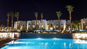 A nighttime view of a hotel with a swimming pool, palm trees, and a castle-like building. - SUNRISE Tucana Resort - Posh Club (Makadi Bay)