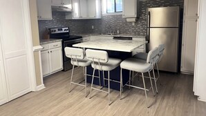 A modern kitchen with white cabinets, a stainless steel refrigerator, a built-in oven, and a bar area with stools.
