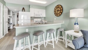 Una cucina con isola centrale, sgabelli da bar, un forno a microonde e una sveglia appesa al muro.