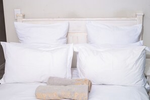 A bed with white bedding and pillows, a folded towel, and a wooden headboard. - 5hrs back up power, Aircon, Uncapped & unlimted WIFI,5km from Blouberg beach.  (Cape Town)
