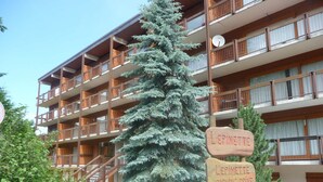 Un immeuble à plusieurs étages, doté de balcons en bois et d’une enseigne indiquant « L’Epinette, parking ».