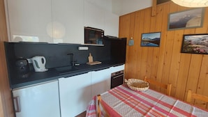 Une cuisine compacte avec un plan de travail noir, un four à micro-ondes, une bouilloire et un évier. On y trouve une table à manger recouverte d’une nappe à rayures et un panier.