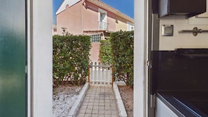 Une porte donnant sur un chemin pavé, une clôture blanche en bois et un bâtiment à la façade rose doté d’un balcon.
