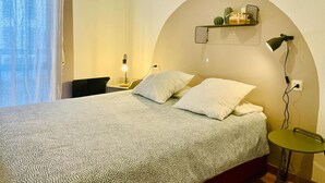 A bedroom with a bed, two bedside lamps, a small table, and a wall-mounted shelf with plants. - Two-Bedroom Apartment with Pool, Balcony, and Garage in Tranquil Jaca (Jaca)