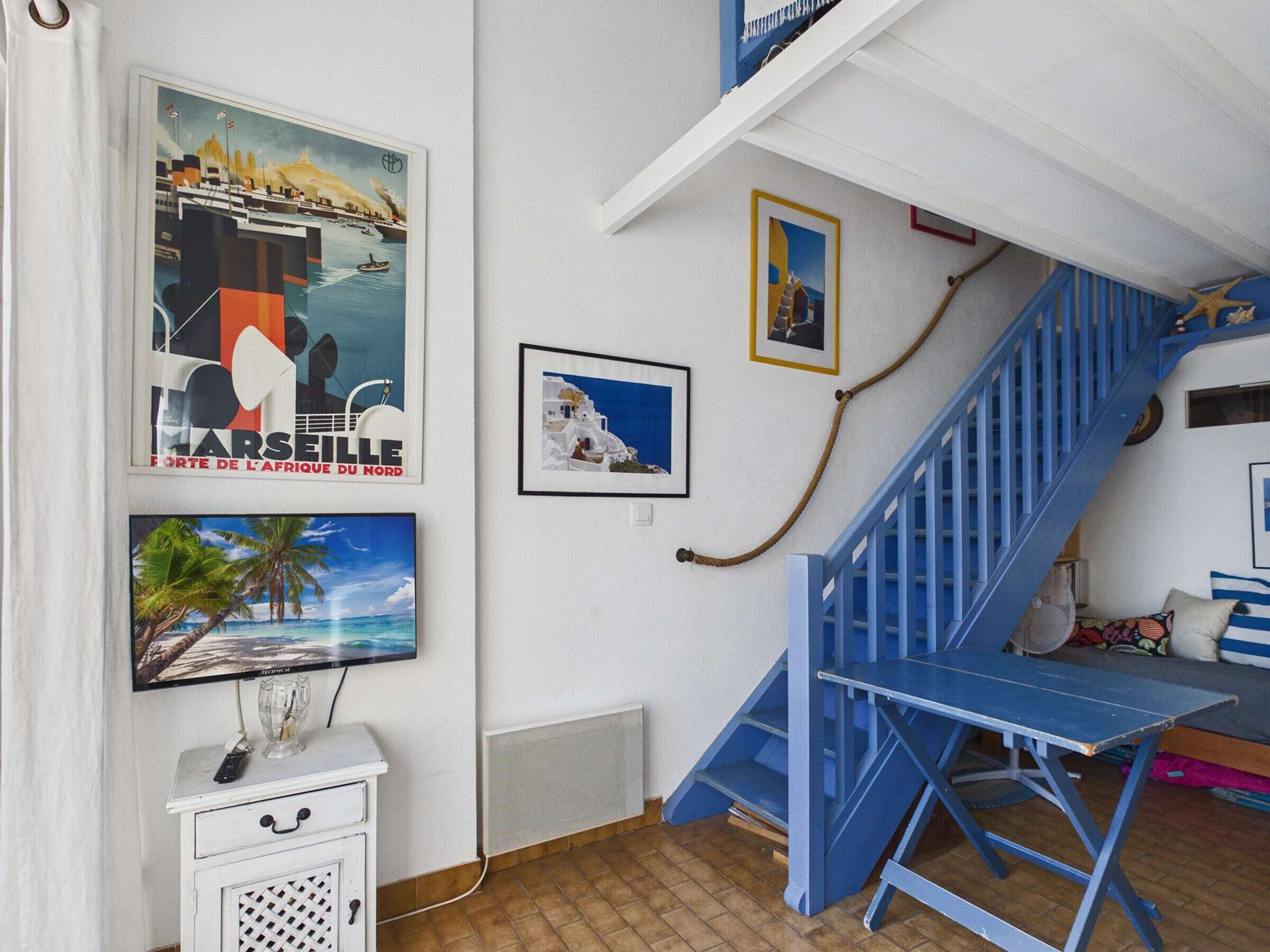 A room with a blue staircase, a white cabinet with a remote control, and three framed pictures on the wall.