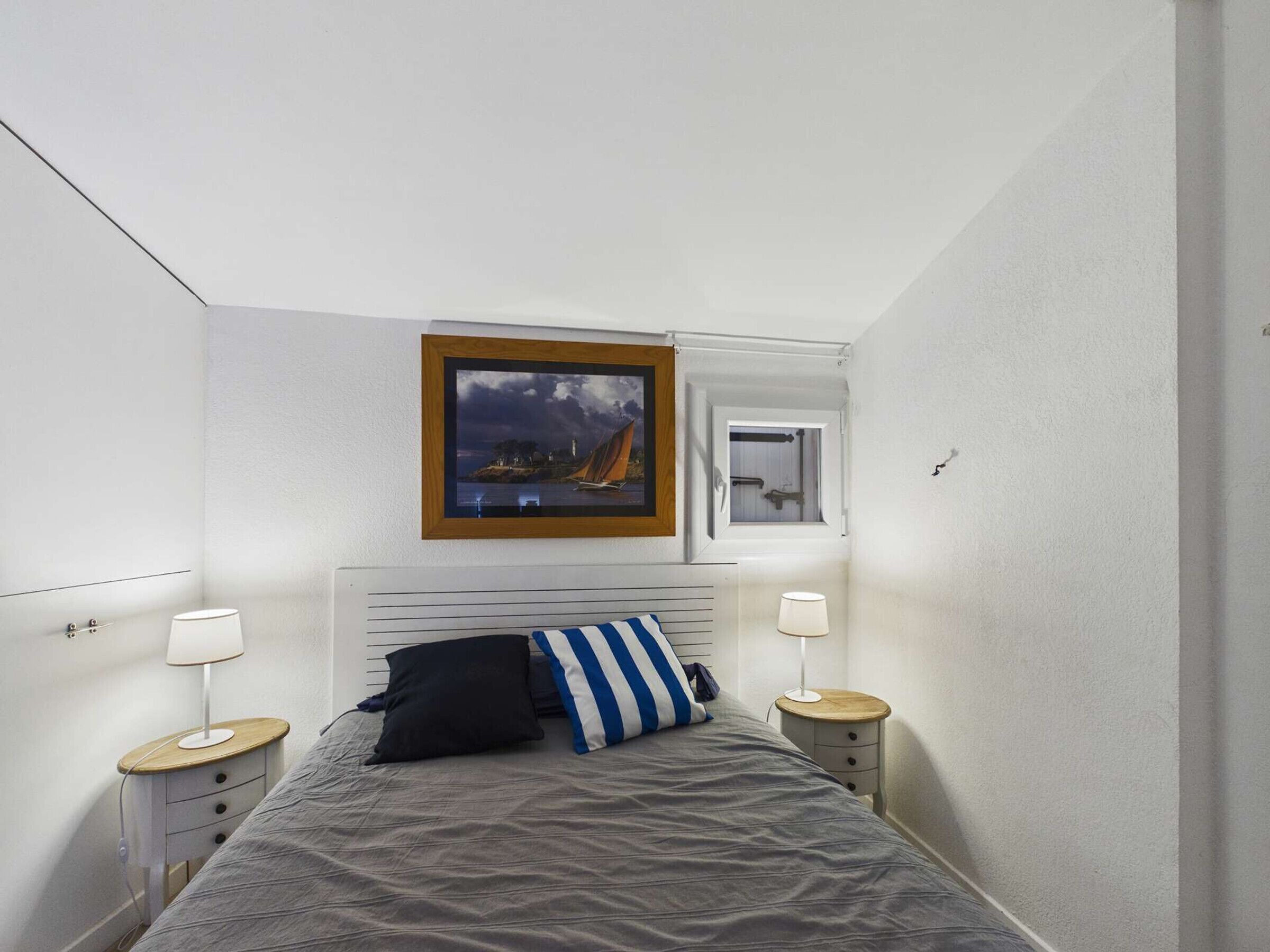 Een slaapkamer met een bed, twee nachtkastjes, een raam met uitzicht en een lijst aan de muur.