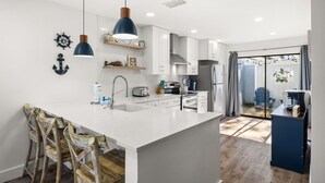 A modern kitchen with white cabinetry, a central island with bar stools, pendant lighting, and a view to a balcony. - Golf Cart ~ Oversized Deck ~ Water & Golf Views (Miramar Beach)
