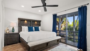 A bedroom with a large bed, wooden headboard, a ceiling fan, a nightstand with drawers, and a view through a glass door to an outdoor deck. - Golf Cart ~ Oversized Deck ~ Water & Golf Views (Miramar Beach)