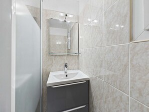 Ein modernes Badezimmer mit Duschkabine aus Glas, einem weißen Waschbecken und einem Spiegel.