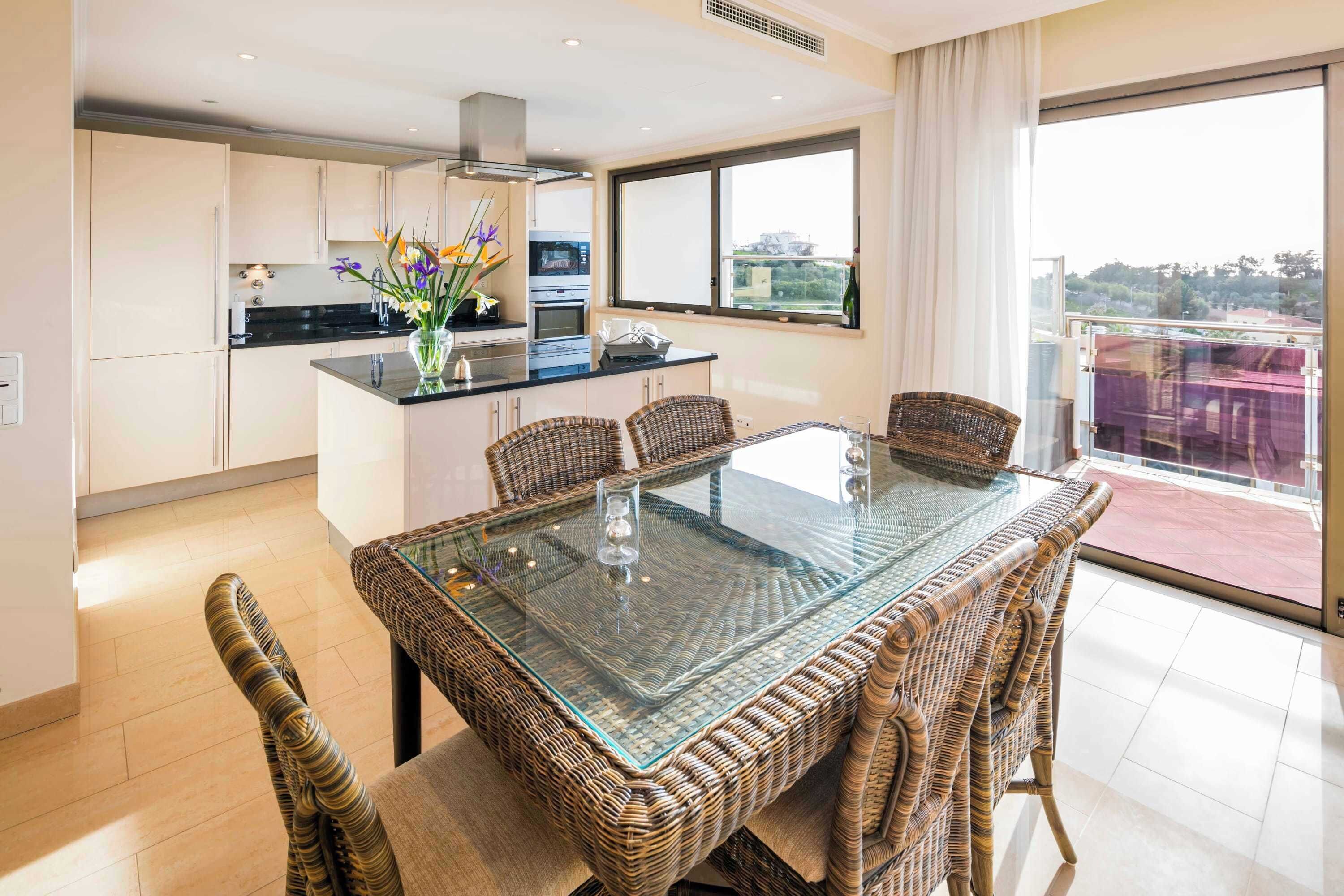 A modern kitchen with white cabinets, a black countertop, and a dining area with wicker chairs and a glass-top table.