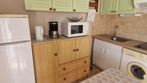 A compact kitchen with a refrigerator, microwave, coffee maker, and washing machine.