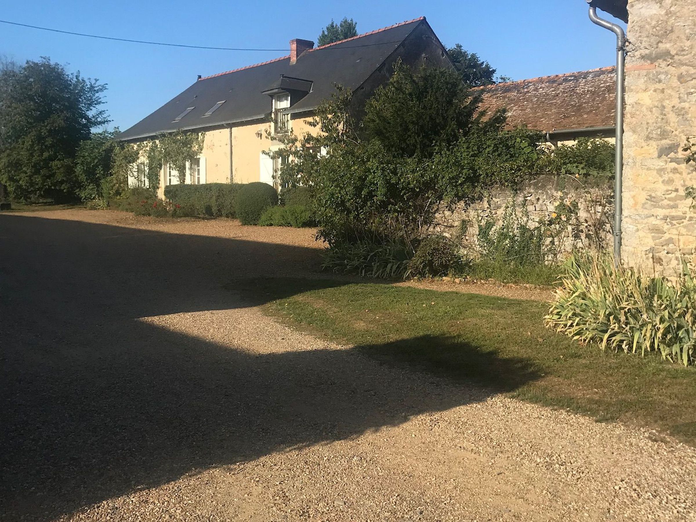 A house with a gravel driveway, a stone wall, and a garden with various plants.