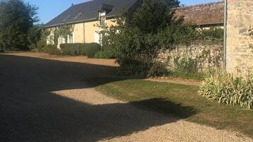 A house with a gravel driveway, a stone wall, and a garden with various plants.