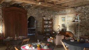 A rustic dining area with stone walls, wooden furniture, and a bookshelf filled with books. - Charming Countryside Retreat with Pool, Near Solesmes Abbey (Solesmes)