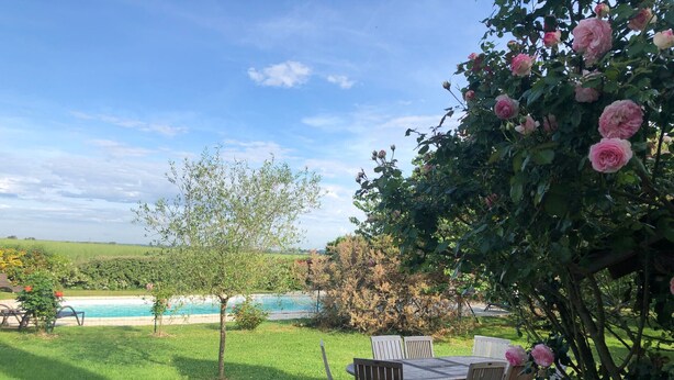 A poolside area with a table and chairs, surrounded by lush greenery and flowering plants. - Charming Countryside Retreat with Pool, Near Solesmes Abbey (Solesmes)