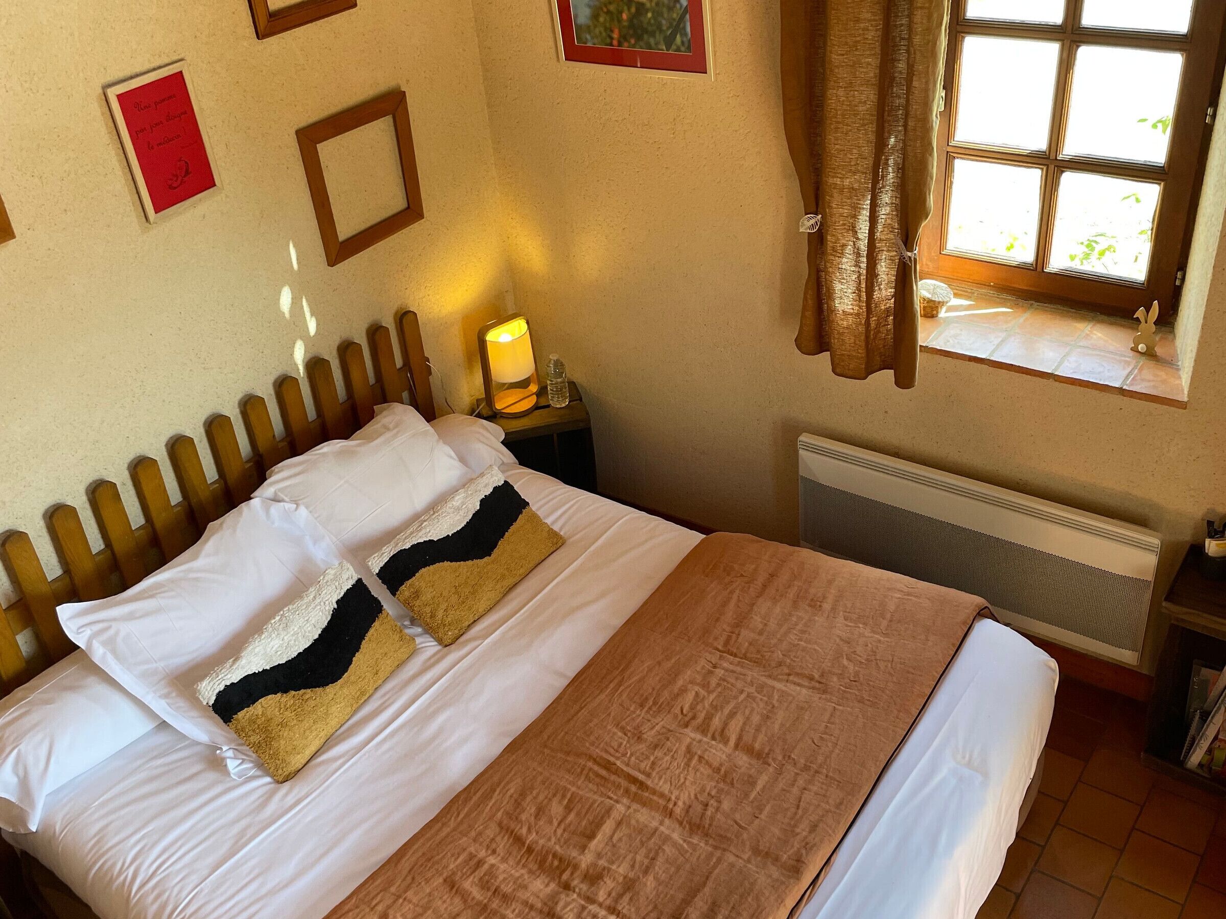Una habitación de hotel con una cama, una mesita de noche con lámpara, una ventana con cortinas y un radiador.