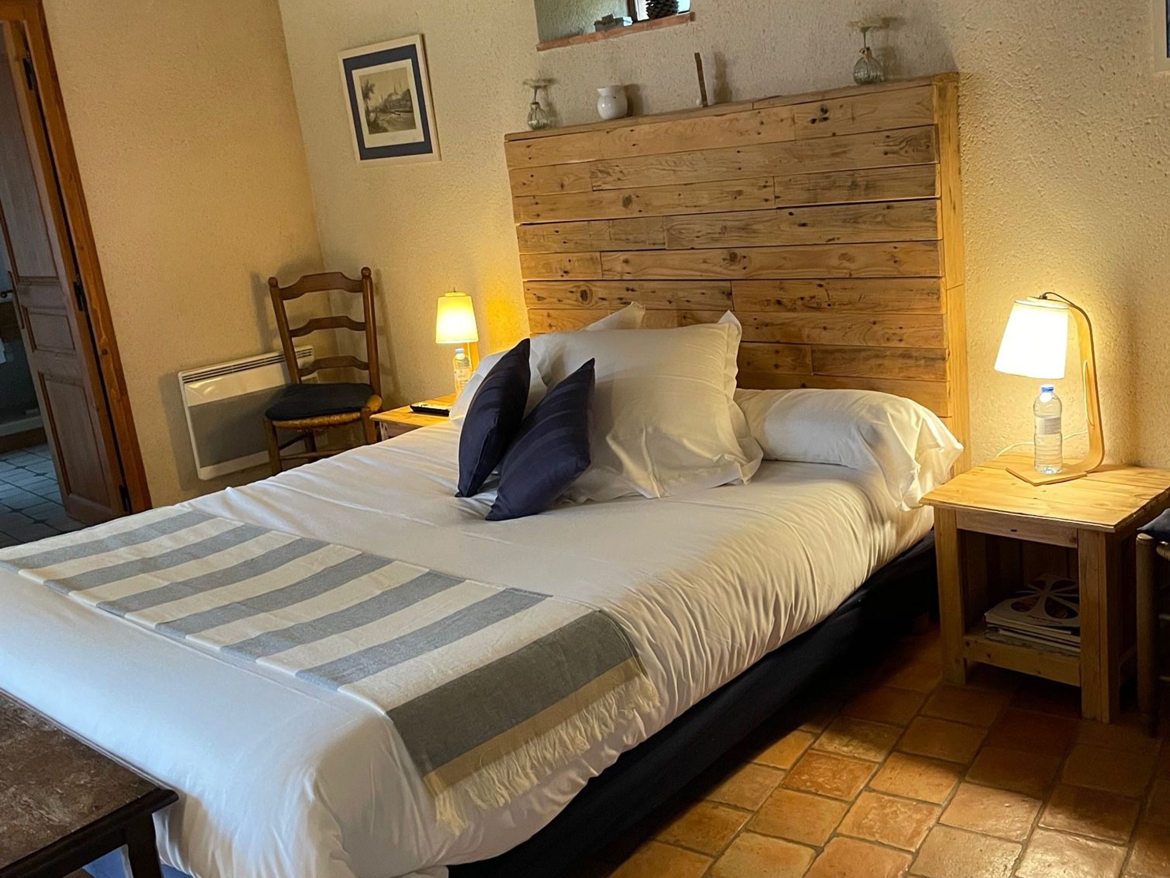 Een net opgemaakt bed met een gestreept deken, een houten hoofdbord en twee bedlampjes.