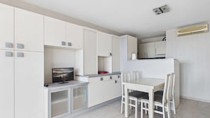 A modern kitchen with white cabinets, a dining table with chairs, and a TV on a cabinet. - Seaside Gem: Air-Conditioned 1-Bedroom Apartment with Ocean View Terrace at Grau d'Agde (Le Grau d'Agde)