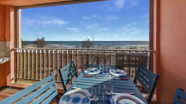 A balcony with a table set for two, overlooking a beach. - Seaside Gem: Air-Conditioned 1-Bedroom Apartment with Ocean View Terrace at Grau d'Agde (Le Grau d'Agde)