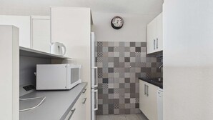 A compact kitchen with white cabinets, a microwave, a kettle, and a patterned backsplash. - Seaside Gem: Air-Conditioned 1-Bedroom Apartment with Ocean View Terrace at Grau d'Agde (Le Grau d'Agde)