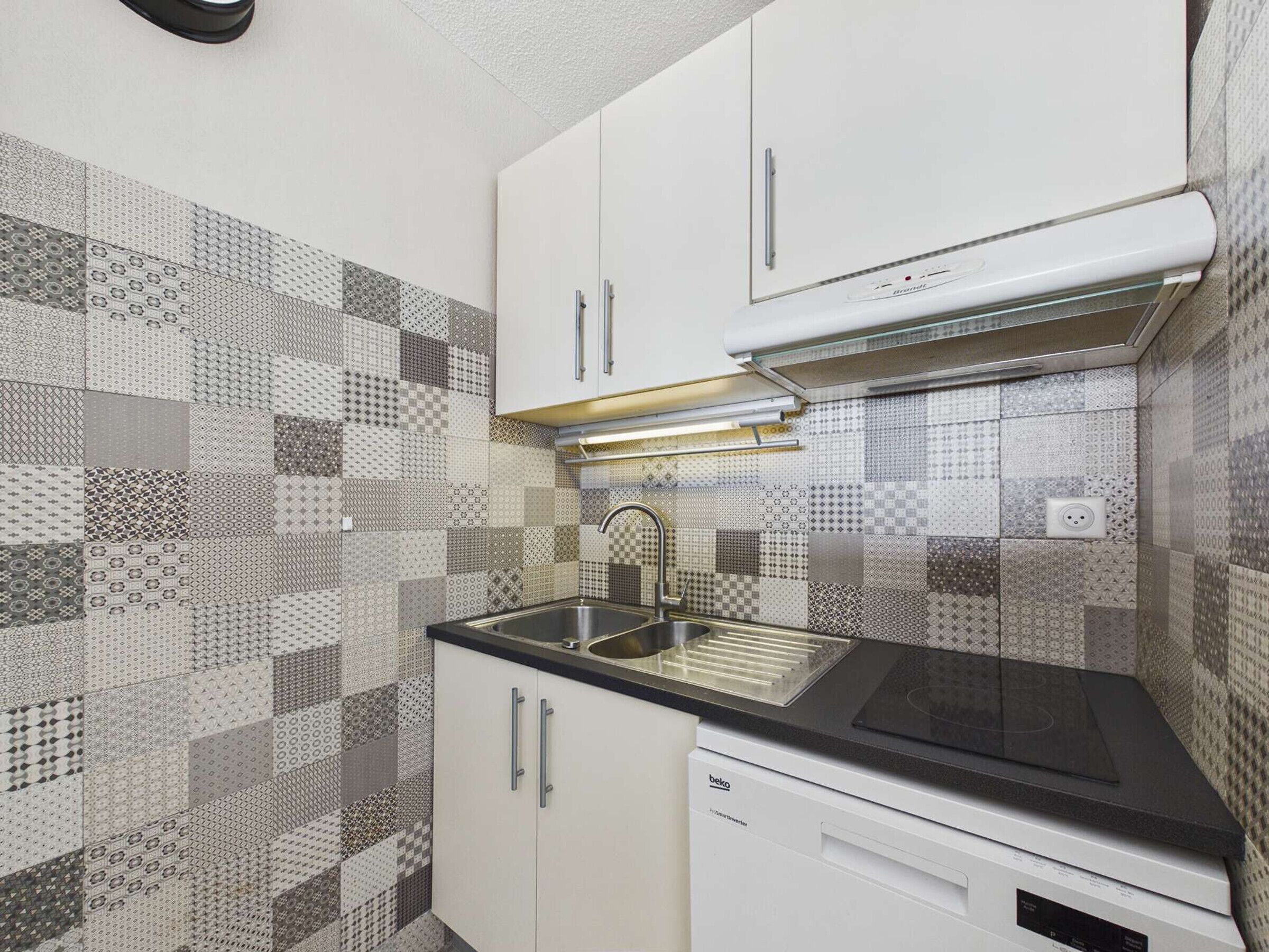 Een keuken met patroon betegelde vloer, een roestvrijstalen spoelbak, witte kastjes en een inbouwoven.