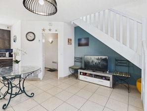 A modern living room with a staircase, a dining area with a glass table, and a TV on a stand.