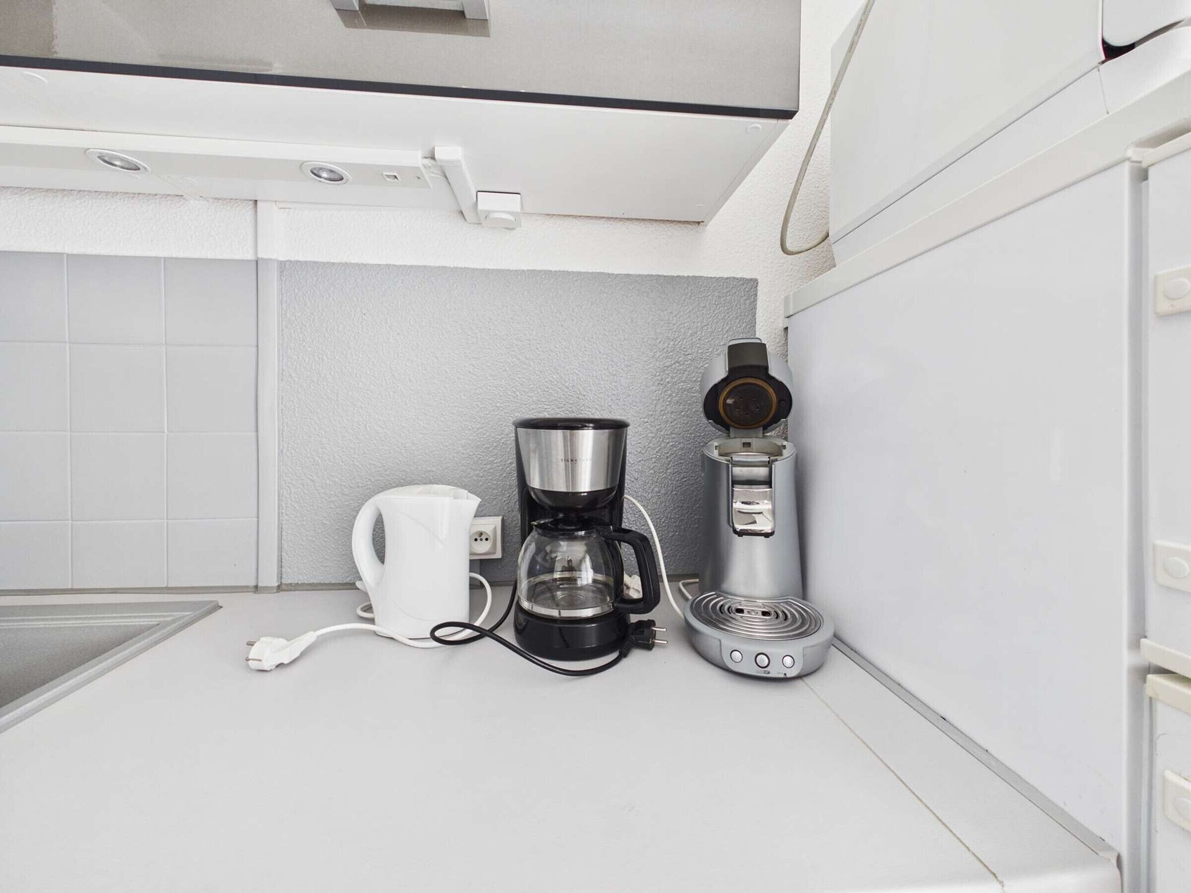 A kitchen with a coffee maker, a kettle, and a countertop.