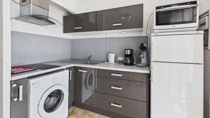 A compact kitchen with a washing machine, a microwave, and a coffee maker. - Cozy 2-Room Apartment for 4 with Pool View, Terrace, and Private Parking (Marseillan-Plage)