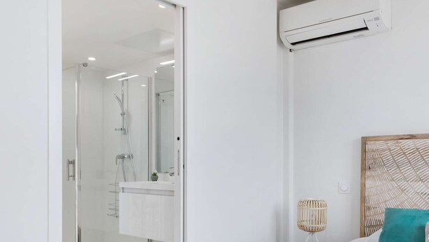 Een moderne slaapkamer met een bed, nachtkastje, wandairconditioner en een badkamer met een douchecabine van glas.