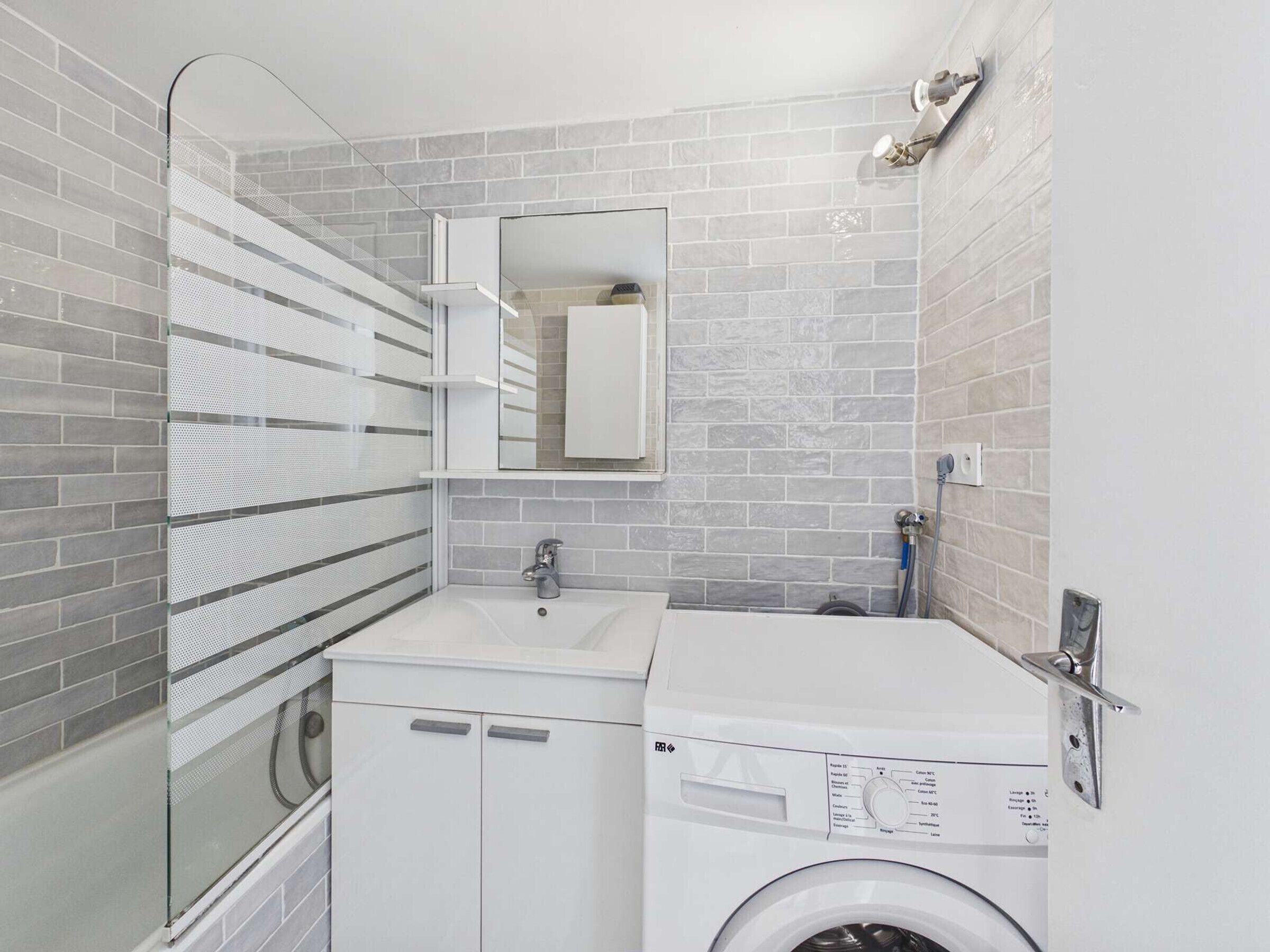 A compact bathroom with a washing machine, a sink, and a mirror.