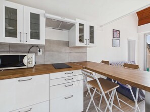 Une cuisine compacte avec des meubles blancs, un four à micro-ondes, une table à manger avec des chaises et un petit coin cuisine.