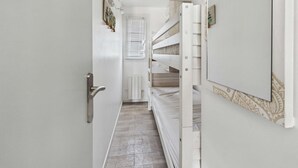 Un pasillo estrecho con una puerta blanca a la izquierda, un radiador blanco y una ventana con persianas.